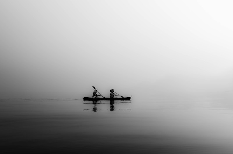 Black and white photo of two people kayaking in the fog